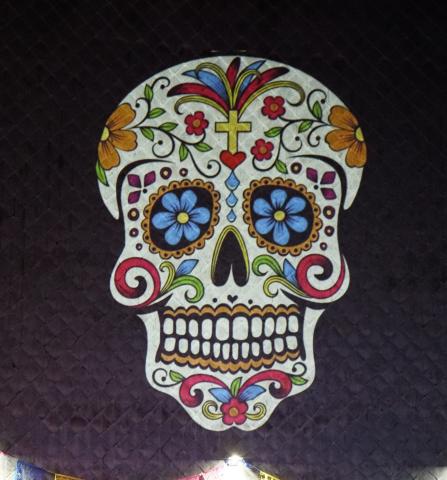 Colorful sugar skull with blue flower eye sockets and floral patterns, on a dark background (Day of the Dead motif).